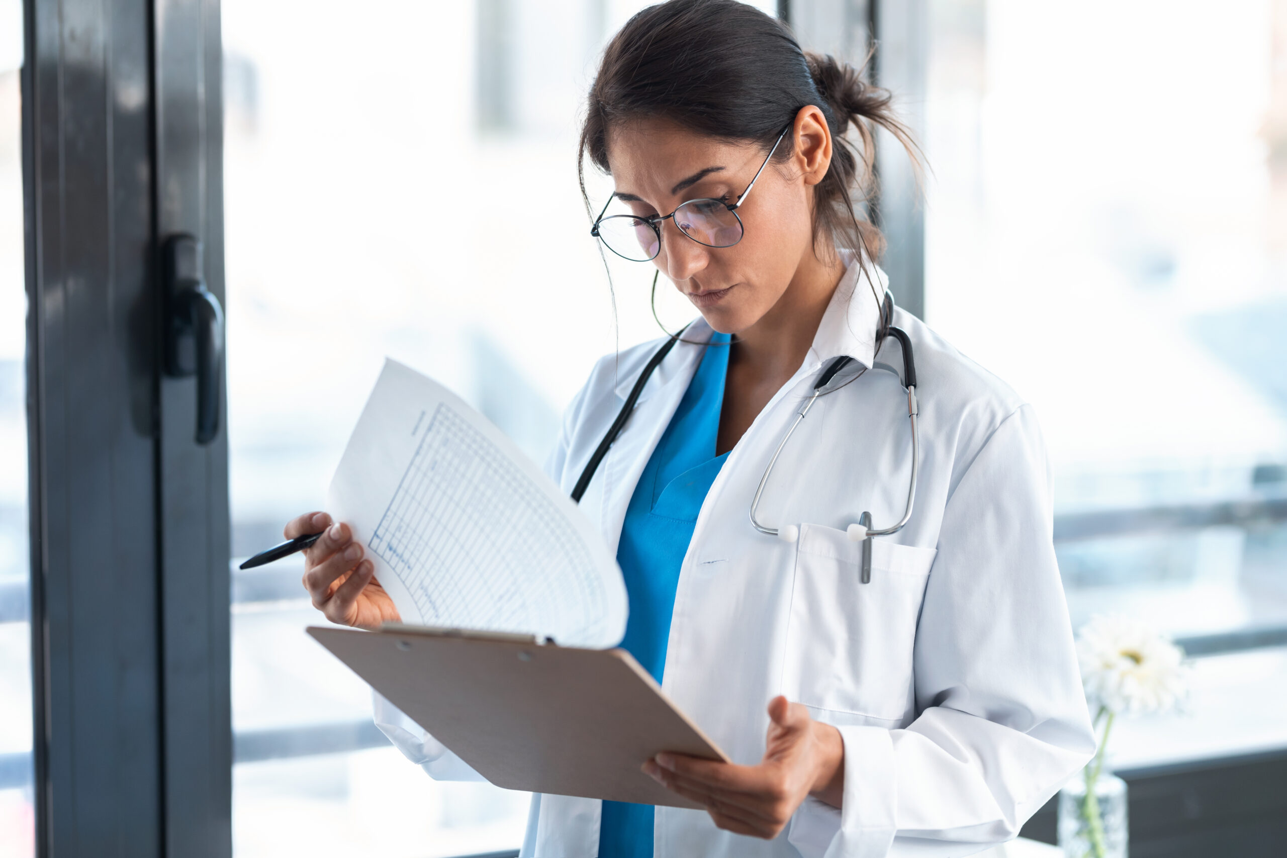 Shot of beautiful female doctor reviewing medical documents while standing in the consultation.